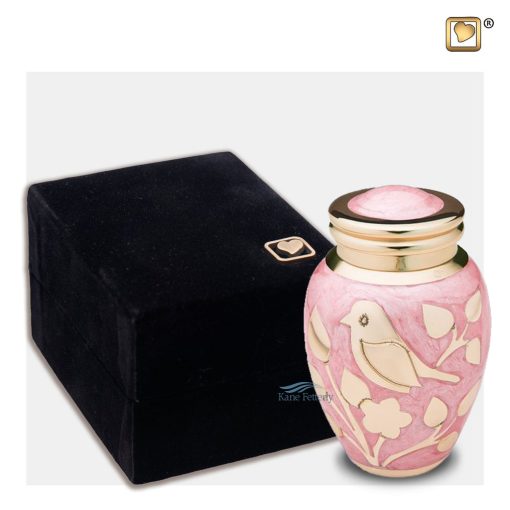 Brass miniature urn with bird and foliage motifs on a pink enamel surface shown with box